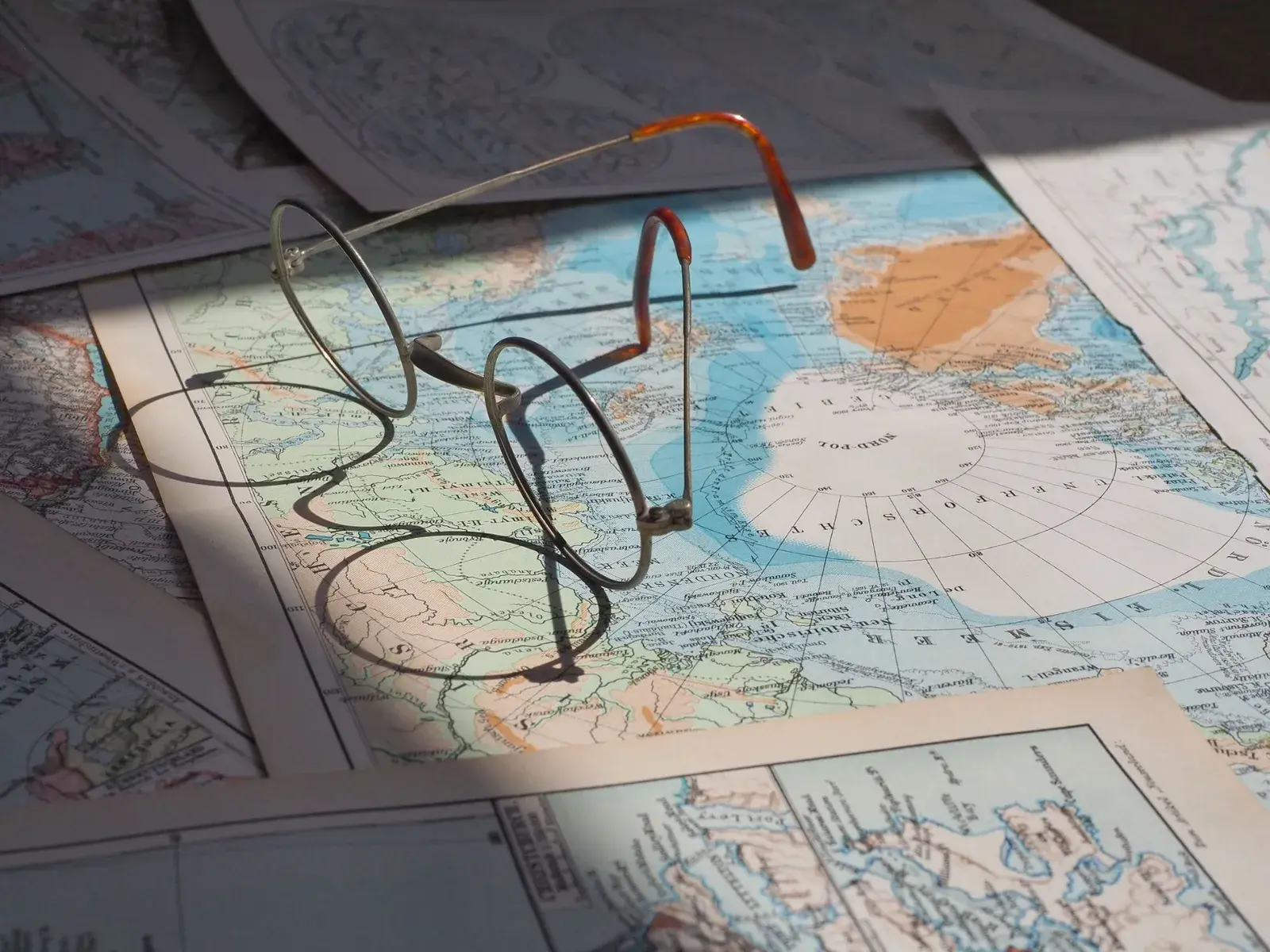 Round wire-rimmed spectacles resting on a spread of vintage printed maps