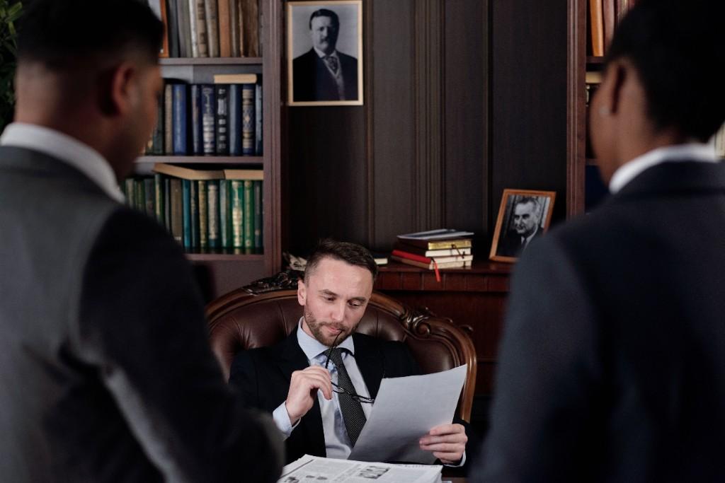 A professional reviewing documents at a desk in a wood-panelled office library during a formal briefing
